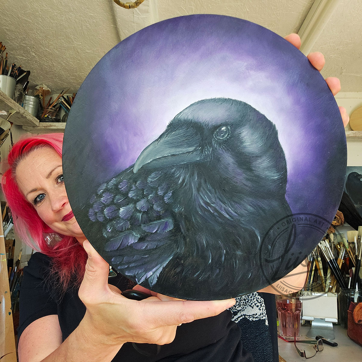Liisa Clark Holding her Original Oil Painting of a Crow with Violet hues part of the Corvid Chroma Series By Liisa Clark
