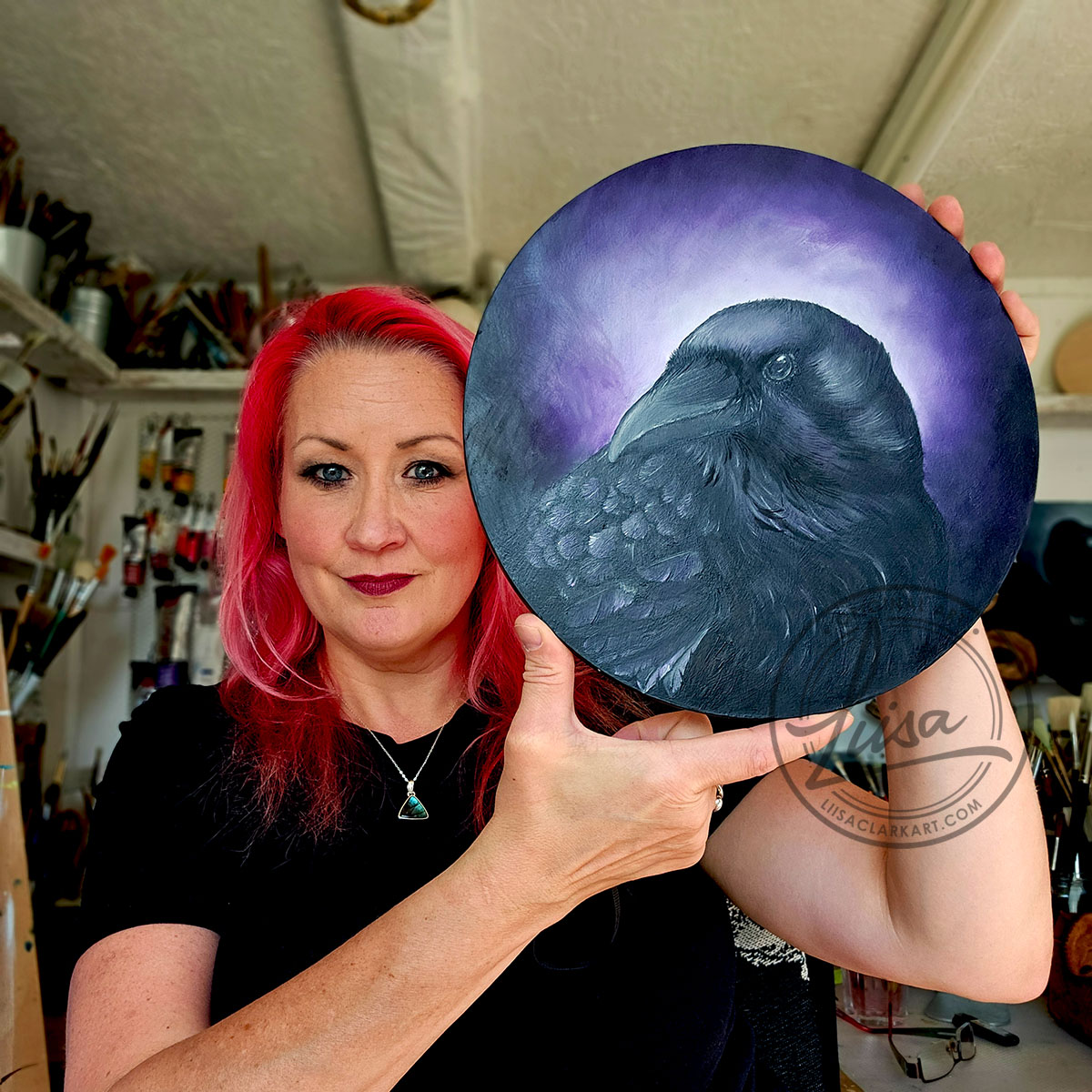 Liisa Clark Holding her Original Oil Painting of a Crow with Violet hues part of the Corvid Chroma Series By Liisa Clark