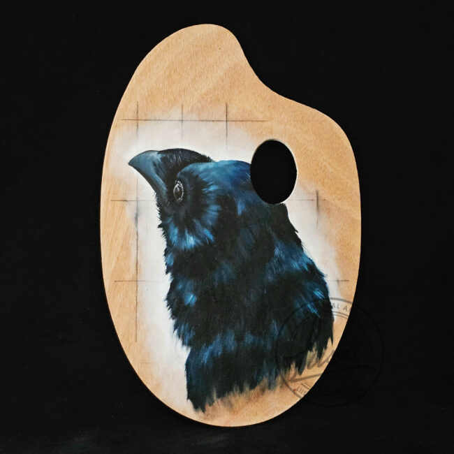 Original crow painting on a wooden artist palette by Liisa Clark, blue-black feathers, black background.