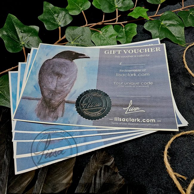 Hand-finished Liisa Clark Art gift voucher featuring original crow artwork, embossed seal and wax detailing, displayed on dark fabric with ivy leaves