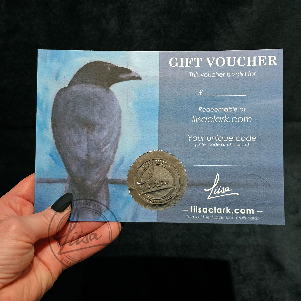 A5 Liisa Clark Art gift voucher held in hand, showing embossed seal and crow artwork design, redeemable online for original artwork and fine art prints
