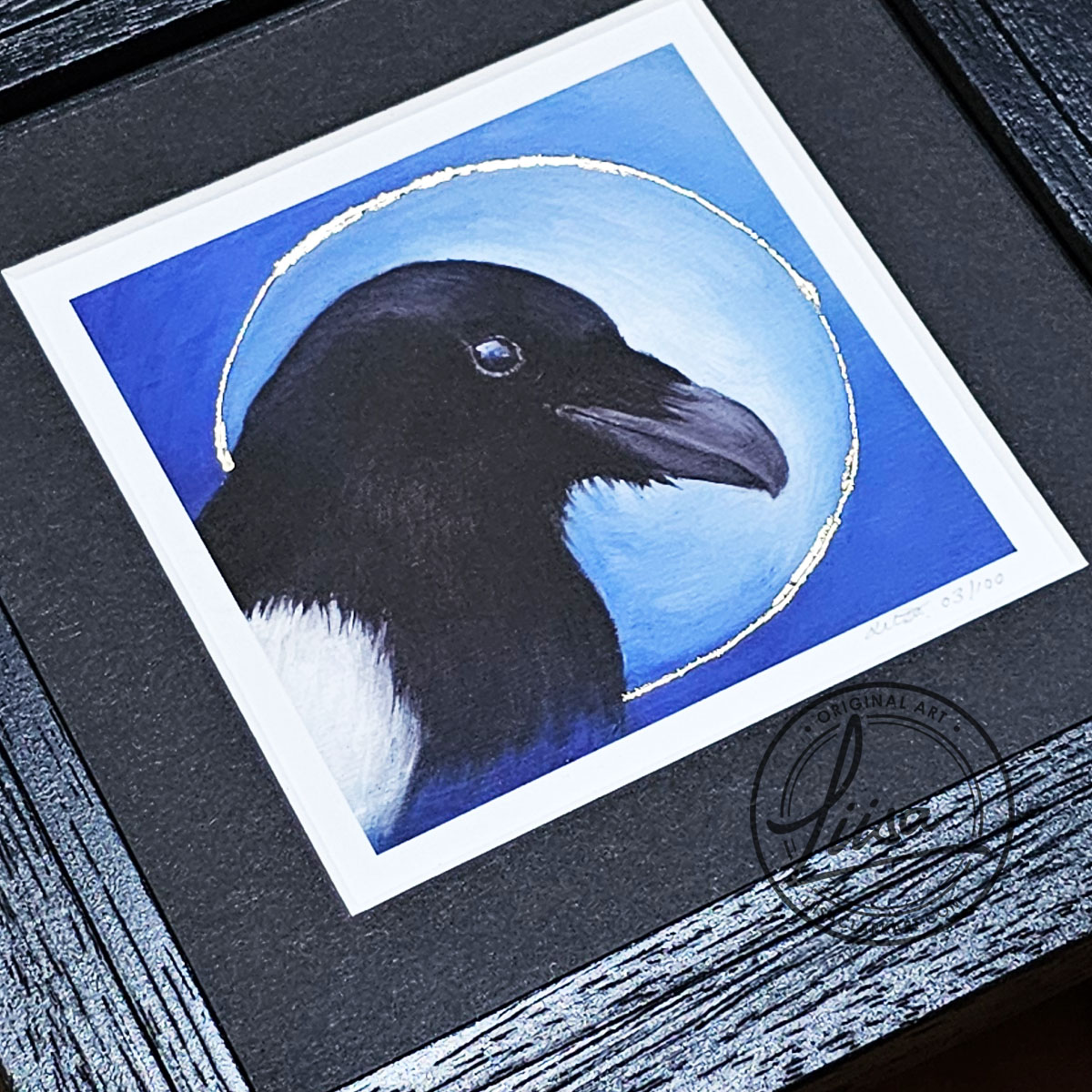 Close-up of hand embellished Gold leaf detailing on a framed magpie giclée print from the Blue Corvid Series by Liisa Clark Art.