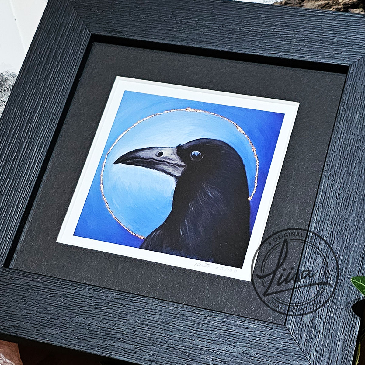 Close-up of a rook portrait print with copper leaf halo detailing from the Blue Corvid Series by Liisa Clark Art.