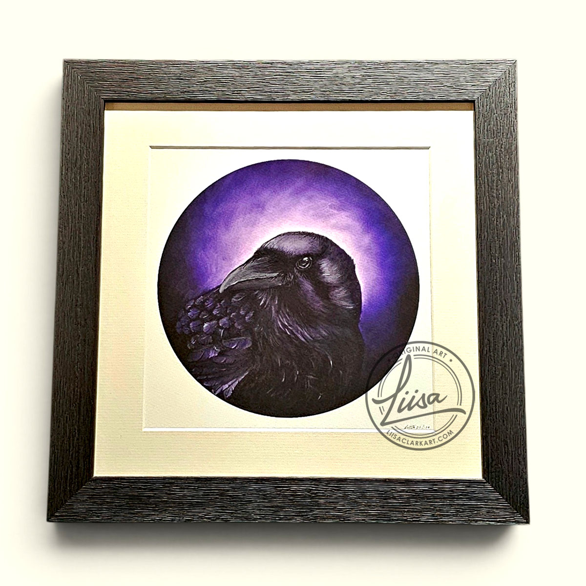Framed circular raven artwork featuring mauve and violet iridescent tones against a glowing purple background, mounted with a white mat inside a textured black wood frame on a plain background