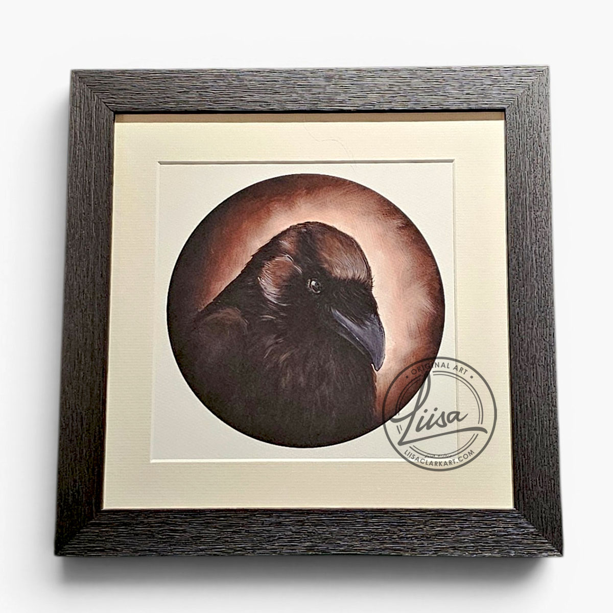 Framed circular raven artwork titled Sepia Storytelling by Liisa Clark Art, featuring warm sepia and bronze tones surrounding a dark raven portrait, mounted with a white mat inside a textured black wood frame.
