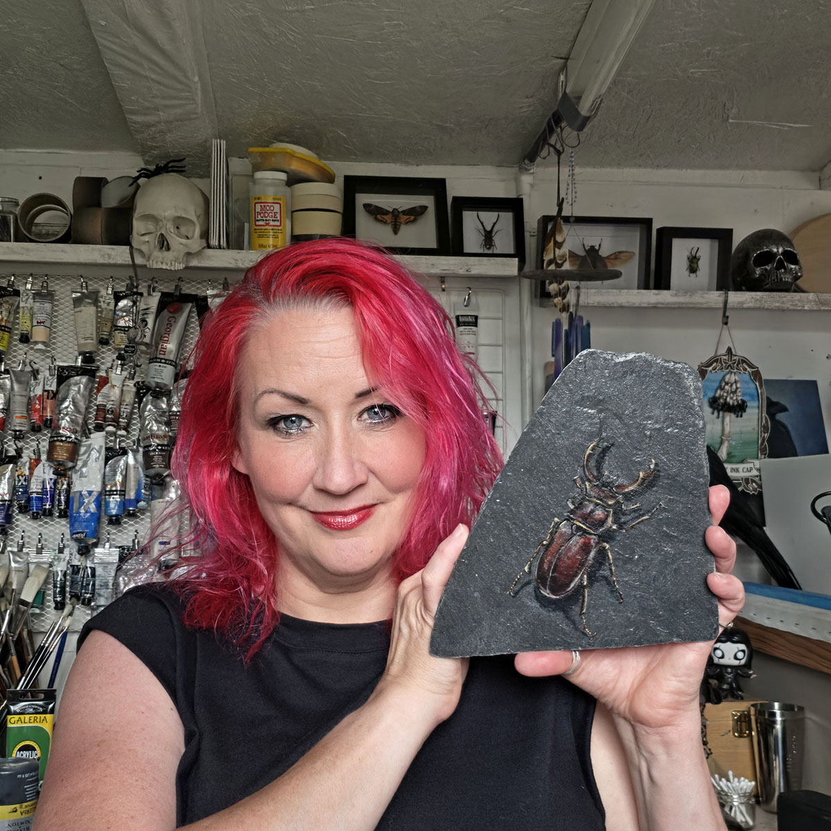 Wildlife artist Liisa Clark holding Keeper of the Old Stone, an original stag beetle painting on genuine reclaimed Welsh slate