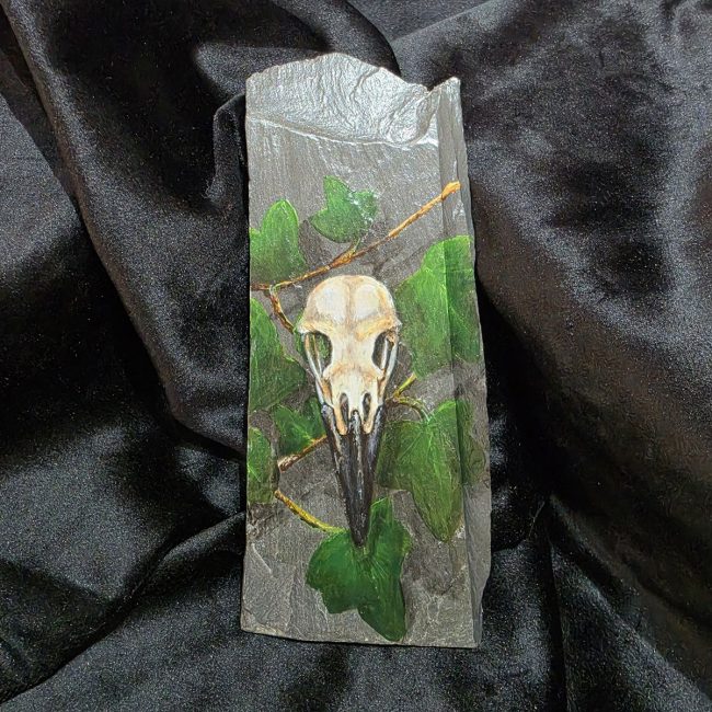 Among Ivy original crow skull painting with green ivy on a piece of reclaimed Welsh slate, photographed against black fabric