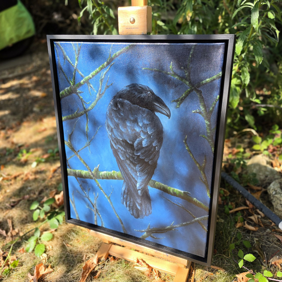 Side angle of framed crow oil painting The Watchful Guardian displayed outdoors