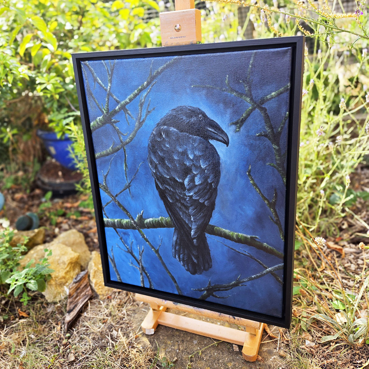 Angled view of The Watchful Guardian original crow painting in a woodland garden setting