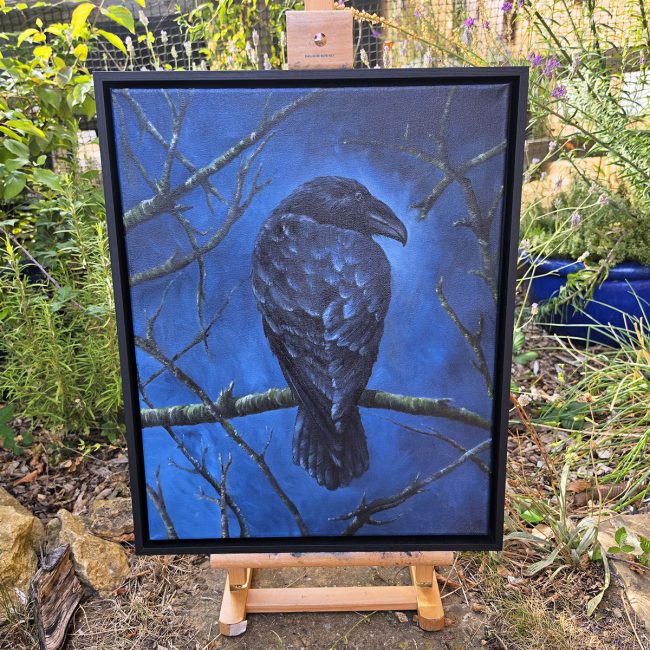 he Watchful Guardian framed crow painting displayed on an easel in a leafy garden