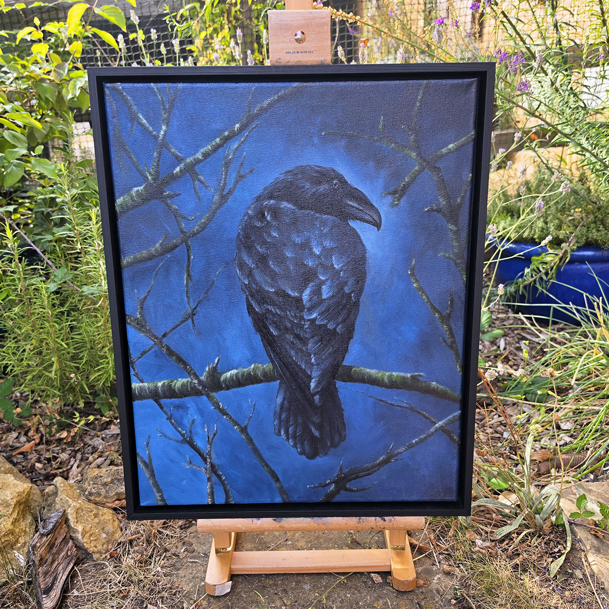 he Watchful Guardian framed crow painting displayed on an easel in a leafy garden