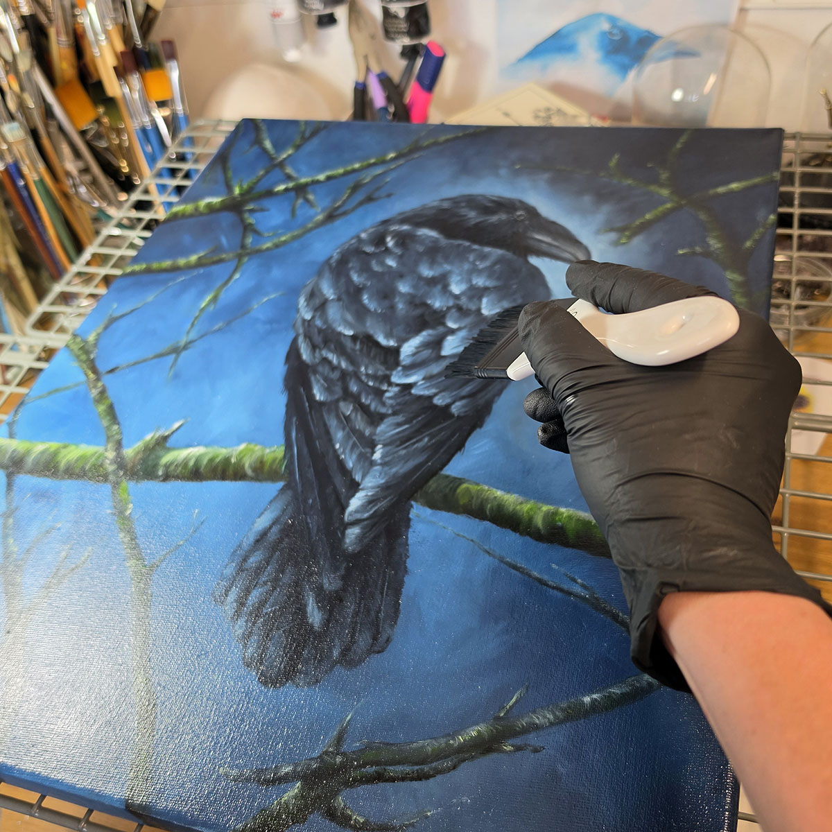 Artist Liisa Clark varnishing The Watchful Guardian original crow oil painting