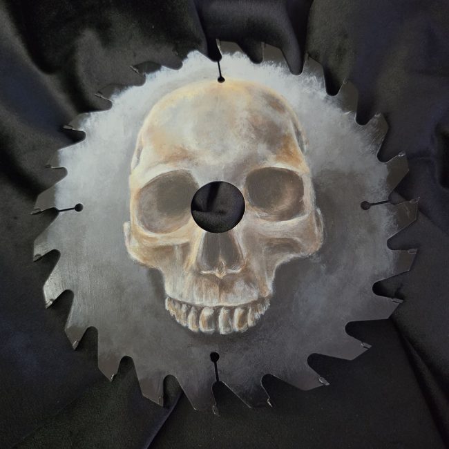Close view of a hand painted human skull on a dark reclaimed vintage circular saw blade.